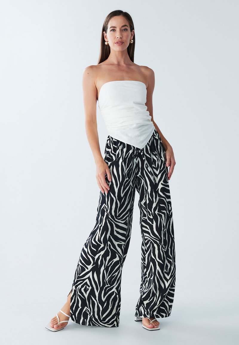 Witte strapless top gecombineerd met zwart-witte zebraprint wijde broek. Glad materiaal met een losse pasvorm en zijsplits voor extra detail.