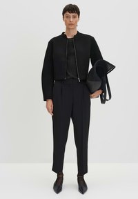 Veste noire cropped avec un col rond, associée à un pantalon noir ajusté. Les accessoires comprennent un sac noir texturé avec des anses.