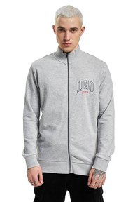 Sivá mikina na zips s vysokým golierom a výšivkou loga "JJ90" na ľavej hrudi; mäkká tkanina s hladkou textúrou.