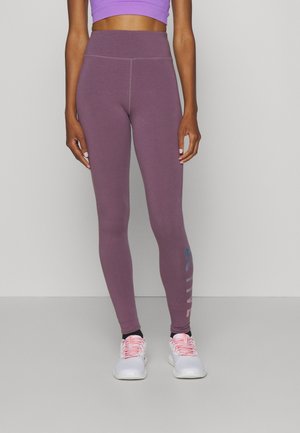 Leggings de sport violets avec une taille haute, texture lisse, et un graphique latéral portant le mot "ACTIVE" en bleu. Portés avec des chaussures de sport blanches.