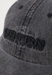 Gray cap made of textured fabric featuring embroidered black letters "URTRN" on the front. Curved brim with stitching details and ventilation holes.
