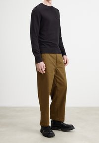 Maglione nero lavorato a maglia con collo tondo, abbinato a pantaloni larghi color sabbia. La modella indossa stivali neri con suola spessa.