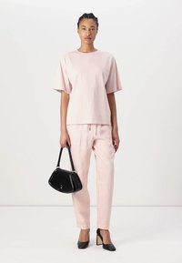 Light pink cotton t-shirt with short sleeves, paired with matching pants. Holds a black handbag and wears black heeled shoes. Simple design.