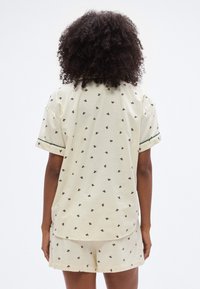 Σετ πιτζάμες βαμβακερές σε κρεμ χρώμα με κοντά μανίκια και σορτς. Διαθέτει μικρό λουλουδάτο μοτίβο και πράσινες λεπτομέρειες στα μανίκια.