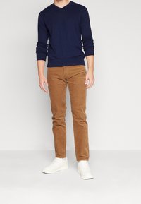 Marinblå V-ringad tröja, bruna manchesterbyxor och vita sneakers. Tröjan har långa ärmar och ribbade muddar, medan byxorna har en texturerad yta.