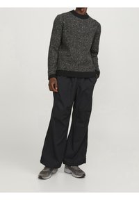 Maglione grigio macchiato con scollo e polsini neri a coste, abbinato a pantaloni neri larghi e sneakers grigie.