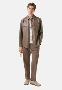 Brun læderjakke med to brystlommer, knaplukning, kombineret med matchende brune bukser og lysebeige sneakers; moderne pasform.