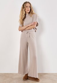 Licht taupe gebreide outfit met een kort mouwtop met een hoge hals en wijde broek, beiden met een zachte, gestructureerde afwerking.