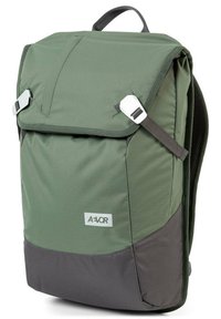 Zielony plecak z klapą zakładaną na wierzch, szarym spodem, regulowanymi paskami i detalem z logo. Wykonany z trwałej, teksturowanej tkaniny.