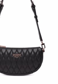 Borsa a tracolla nera trapuntata in pelle sintetica, caratterizzata da una forma curva, spallaccio regolabile e hardware in oro rosa. Logo del brand visibile.