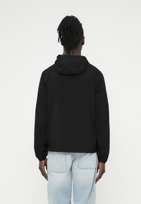 Μαύρο ελαφρύ μπουφάν με κουκούλα, μακριά μανίκια και ελαστικές μανσέτες. Κομμένο σε άνετη γραμμή με απαλό ύψος.