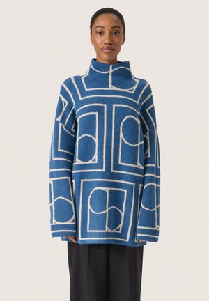Blauer Wollmischpullover mit hohem Kragen, der ein geometrisches weißes Muster und übergroße Ärmel aufweist. Strukturierte Oberfläche mit lockerer Passform.
