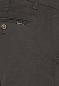 Tasca dei pantaloni grigi scuri con un bottone nero e una piccola etichetta "Pepe Jeans" cucita sopra l'apertura della tasca.