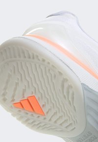 Άσπρη αθλητική σόλα παπουτσιού με υφή από καουτσούκ και μοτίβο λαβής, με διαφανές πορτοκαλί διακοσμητικό και πορτοκαλί λογότυπο με τρεις ρίγες.