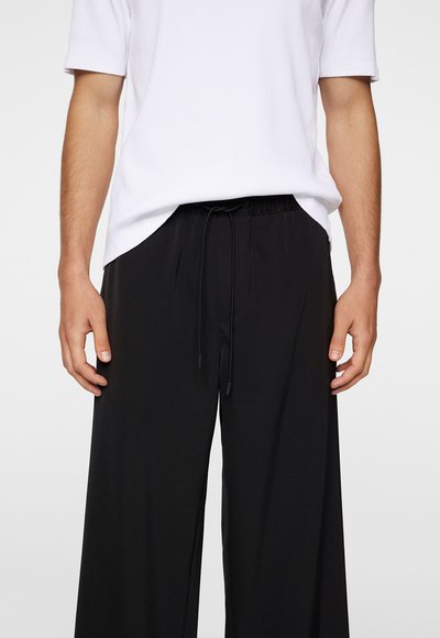 Black wide-leg pants with a drawstring waistband, featuring a smooth texture. Worn with a loose-fitting white t-shirt.