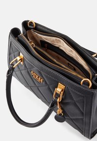 Sac à main noir matelassé en cuir texturé, doté de ferrures dorées, d'une fermeture éclair supérieure et d'une doublure en tissu avec des poches intérieures.