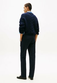 Maglione azzurro a trecce dal tessuto spesso, indossato sopra una camicia azzurro chiaro. Abbinato a pantaloni scuri e mocassini neri.