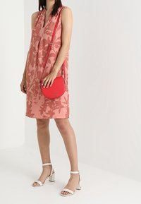 Rosa, blumenmuster-bedeckte, ärmellose Kleid, kombiniert mit einer roten, runden Umhängetasche und weißen Blockabsatzsandalen. Glatter Stoff.