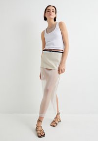 Hvid top, beige nederdelsoverdel, gennemsigtig lang nederdel, sort og brun bælte, remsandaler med en struktureret overflade.