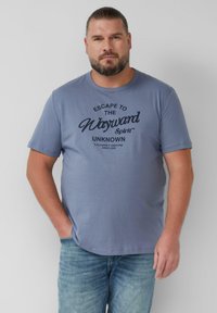 Hellblaues Baumwoll-T-Shirt mit kurzen Ärmeln, das auf der Vorderseite einen schwarzen Aufdruck mit der Aufschrift "Escape to the Wayward Spirit" zeigt.