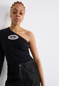 Sort, ribbet one-shoulder topp med en sirkulær Adidas-logo på brystet, kombinert med høyt liv svarte denim bukser med lommer.