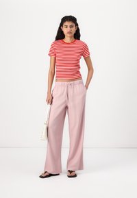 Chemise à manches courtes rayée rouge et blanche associée à un pantalon large rose pâle avec une taille élastique. Sandales plates noires et sac blanc.