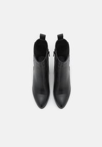 Un par de botines de cuero negro con puntas afiladas, cremalleras laterales y tiradores, mostrados desde arriba sobre un fondo blanco.