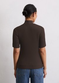Haut marron à manches courtes côtelé avec un col montant, forme ajustée et texture lisse, associé à un jean en denim bleu clair.