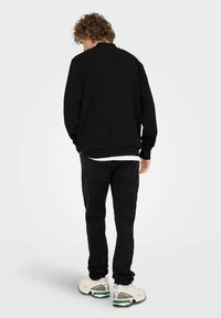 Sort sweatshirt med klassisk rund hals, parret med sorte jeans. Løs pasform med et tekstureret stof. Fodtøjet har et beige og grønt design.