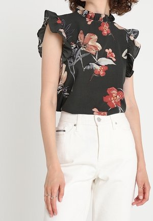 Schwarze Bluse mit floralen Mustern und Rüschensäumen, verziert mit lebhaften roten und beigen Blumen, kombiniert mit weißen weiten Hosen. Glatte Stoffstruktur.