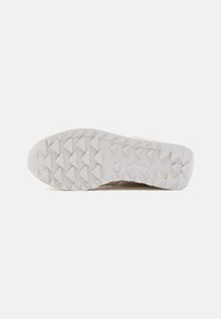 Suola della scarpa con una superficie in gomma bianca caratterizzata da pattern di suola a forma di triangolo per la trazione e il logo Saucony nella zona del tallone.