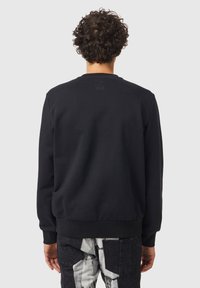 Felpa nera in misto cotone con collo e polsini a coste. Presenta una piccola patch con logo sulla parte superiore della schiena. Vestibilità casual.