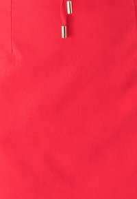 Punane kangast seelik, millel on sile tekstuur, nöörkinnitusdetail ja nööriotsas metallist aksendid.