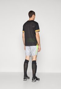 Sort atletik skjorte med guld accenter, grå shorts med et subtilt mønster og neongrøn side detalje, parret med sorte knæstrømper og sko.