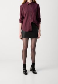 Camisa abotonada burdeos con un patrón de lunares, combinada con una mini falda de cuero negra, medias transparentes y zapatos Mary Jane de charol negros.