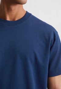 Donkerblauw T-shirt met ronde hals en korte mouwen, gemaakt van gladde katoenstof, met een geribbelde halslijn en minimale stikseldetails.