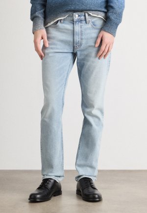 Light blue denim jeans with a straight leg fit, featuring a classic five-pocket design, zipper fly, and subtle fading. Worn with black shoes.