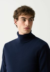 Jūras tumši zilas krēmveida kakla džemperis, izgatavots no mīksta adīta auduma, ar cieši pieguļošu kaklu un garām piedurknēm, gludu tekstūru un minimālistisku dizainu.