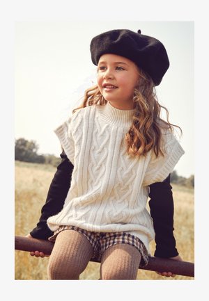 Crème kabelgebreide trui met korte mouwen, gedragen over een zwart longsleeve top. Bruine geruite shorts en getextureerde maillots. Zwarte baret als accent.