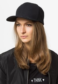 Schwarze Mütze aus Stoff mit strukturiertem Design und flacher Krempe. Hat dezente Markenkennzeichnung auf der Vorderseite und wird mit einer schwarzen Bomberjacke kombiniert.