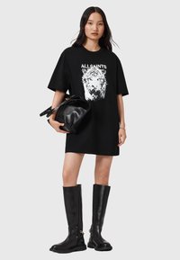 Vestido camiseta negro oversize con un gráfico blanco de un tigre, combinado con botas de cuero negras hasta la rodilla y un bolso negro. Texturas suaves.