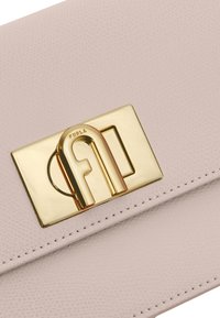 Portafoglio in pelle rosa chiaro con una finitura testurizzata e un grande fermaglio dorato con un logo stilizzato e forma rettangolare.