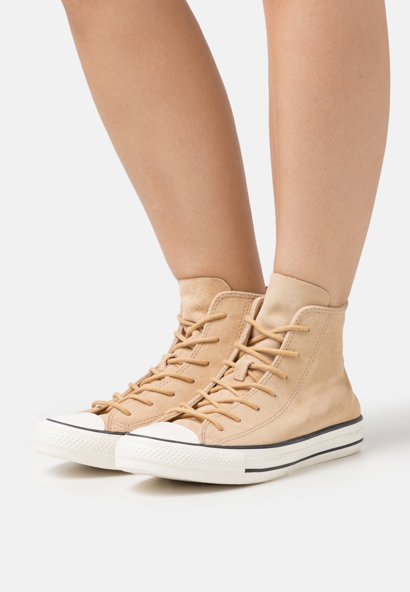 Adidași bej, tip high-top, din suede, cu vârf și talpă din cauciuc alb, având șireturi și o textură specială.