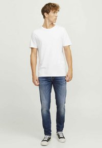 White cotton t-shirt with short sleeves; paired with blue denim jeans featuring a slight fade. Shoes are black sneakers with white accents.