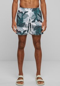 Maillots de bain avec une base blanche ornée de motifs de feuilles tropicales vertes et noires, ceinture élastique et cordon ajustable.