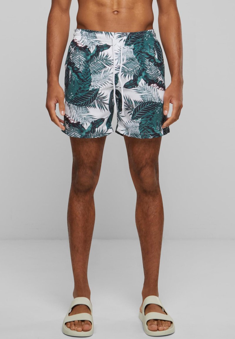 Maillots de bain avec une base blanche ornée de motifs de feuilles tropicales vertes et noires, ceinture élastique et cordon ajustable.