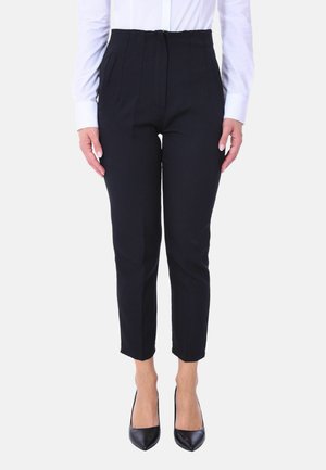 Pantaloni neri sartoriali con vita alta, pince e tasche laterali. Indossati con una camicia bianca e décolleté neri a punta. Texture liscia.