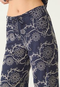 Marineblauwe broek met witte bloemenborduursels en een voorste koord dat in een strik is geknoopt, gedragen op de onderlichaam en benen van een persoon.