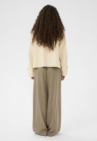Bež kratka jakna z dolgimi rokavi, kombinirana z ohlapnimi, širokimi hlačami v kaki barvi. Mehka tekstura, minimalističen dizajn.