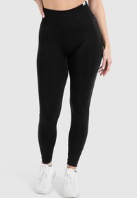 Svarta högmidjade leggings med en mjuk textur, som har en bred midjeresår och en slät design, kombinerat med vita sportskor.
